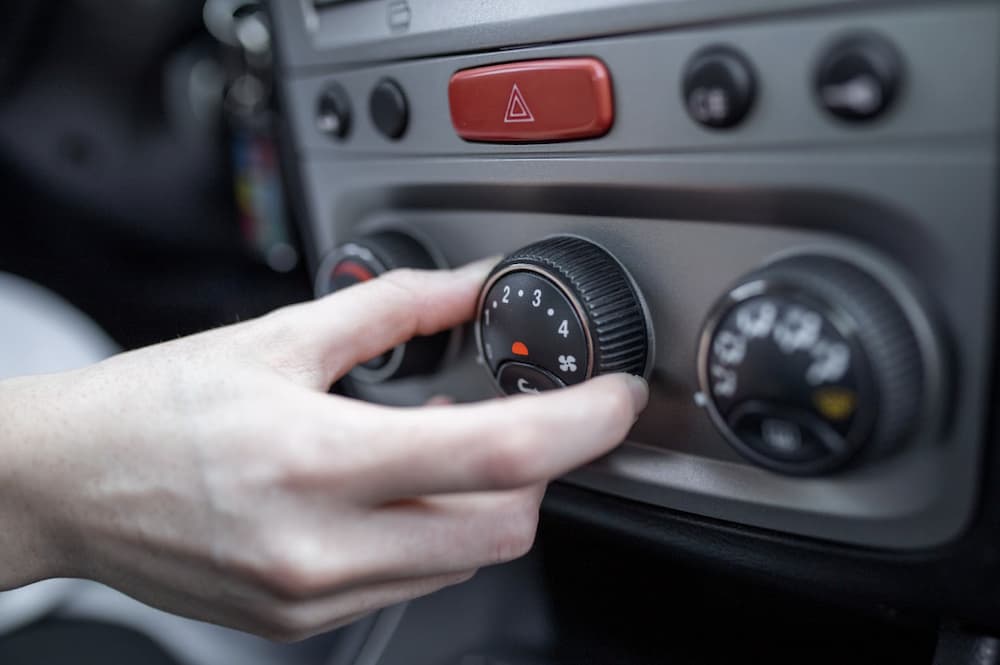 Person turning air conditioning knob while A/C blows hot air